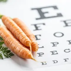 Marchewki, bogate w beta-karoten i zeaksantynę, leżą obok tablicy Snellena, symbolizując zdrowie oczu.