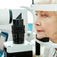 Starsza kobieta podczas badania wzroku przy użyciu sprzętu okulistycznego.