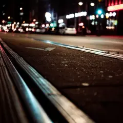 Torowisko tramwajowe w nocy, rozmyte światła miasta w tle.