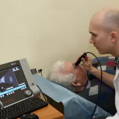 Lekarz wykonuje badanie usg oka u pacjenta leżącego na kozetce. Na ekranie aparatu widoczny jest obraz oka.