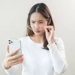 Kobieta w okularach z trudem patrzy na ekran telefonu.