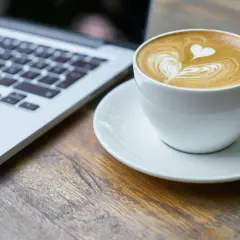 Kawa latte z sercem na piance obok laptopa. Idealny moment na relaks i picie kawy po operacji zaćmy.
