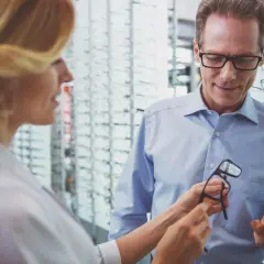 Optometrysta pomaga mężczyźnie wybrać okulary w salonie optycznym.