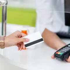 Dłoń z kartą zbliża się do terminala płatniczego.