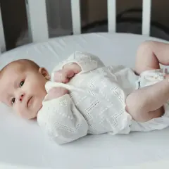 Noworodek w białej koszulce leży w łóżeczku, a ręce rodzica dotykają jego stóp.