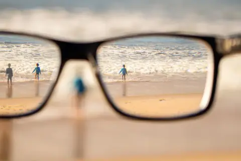 Okulary korygujące widok na plażę z dziećmi wchodzącymi do morza.