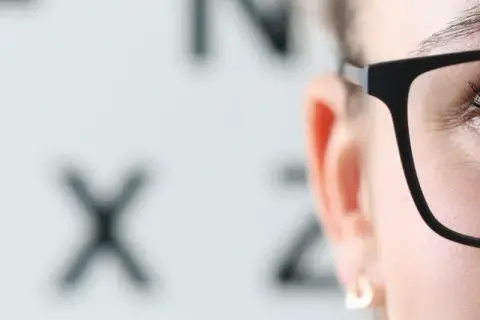 Kiedy dobrać okulary po operacji zaćmy? Zbliżenie na oko w okularach, w tle tablica Snellena.