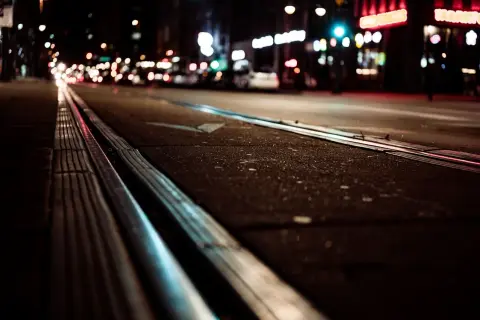 Torowisko tramwajowe w nocy, rozmyte światła miasta w tle.