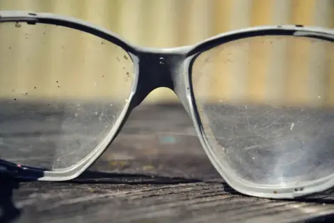 Brudne okulary ochronne leżą na drewnianej powierzchni. Czas na polerowanie okularów, by znów były przejrzyste.
