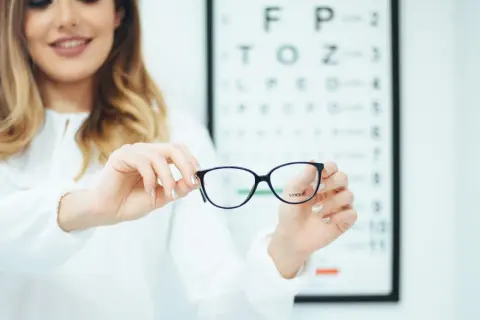 Okulary progresywne dla osób z astygmatyzmem. Optometrystka prezentuje okulary na tle tablicy Snellena.