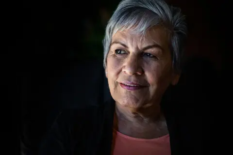 Portret starszej kobiety z siwymi włosami, patrzącej w bok z lekkim uśmiechem.
