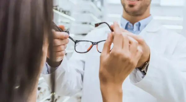 Optometrysta pokazuje okulary klientce. Dowiedz się, ile wynosi dofinansowanie do okularów przez pracodawcę.