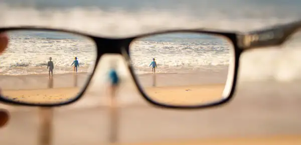 Okulary korygujące widok na plażę z dziećmi wchodzącymi do morza.