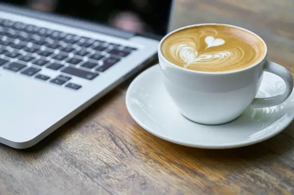 Kawa latte z sercem na piance obok laptopa. Idealny moment na relaks i picie kawy po operacji zaćmy.