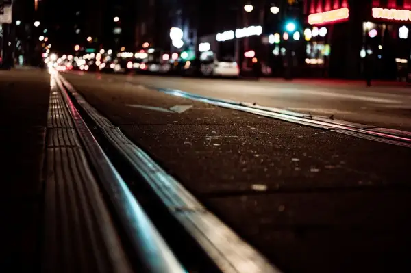 Nocne miasto z torami tramwajowymi. Światła samochodów i neonów tworzą magiczną poświatę, która umożliwia widzenie w ciemności.