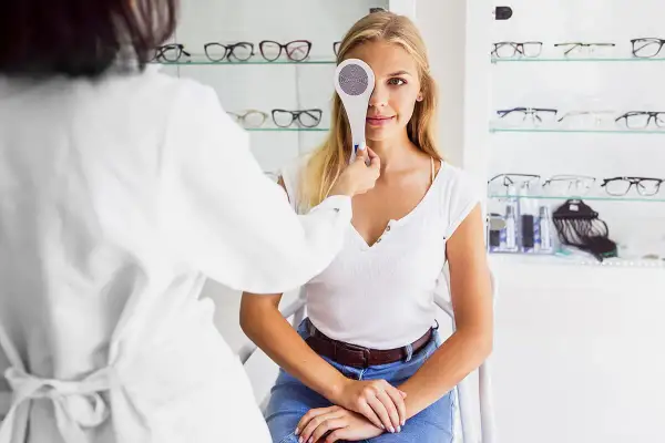 Kobieta przechodzi badanie wzroku, zasłonięte jedno oko. Optometrysta wykonuje cover test.
