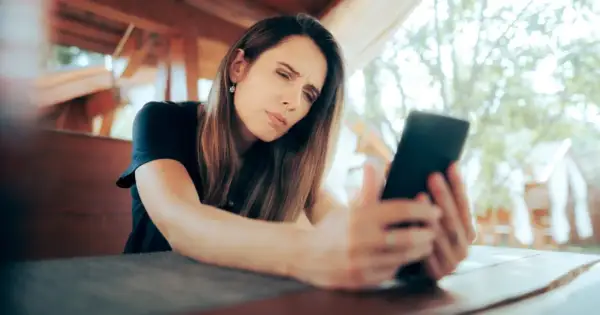 Kobieta z trudem patrzy na ekran telefonu, marszcząc czoło.