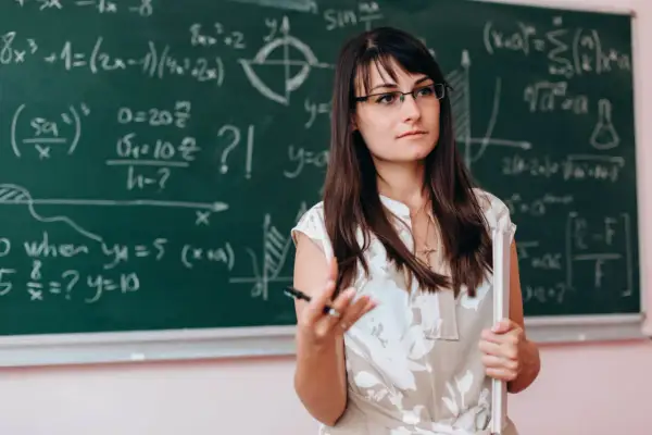 Nauczycielka matematyki w okularach, wyjaśniająca wzory na tablicy. Dofinansowanie do okularów dla nauczycieli to ważna sprawa.