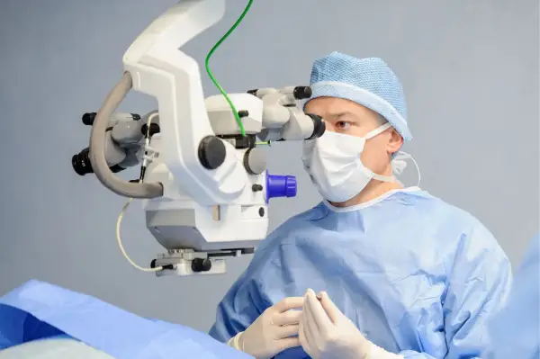 Chirurg w masce i czepku operacyjnym wykonuje trabekulektomię, używając mikroskopu.